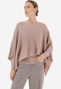 Světle růžový oversized pletený svetr se elegantně splétá, má ribbované textury a široké rukávy, a je spárován s kostkovanými kalhotami na míru.