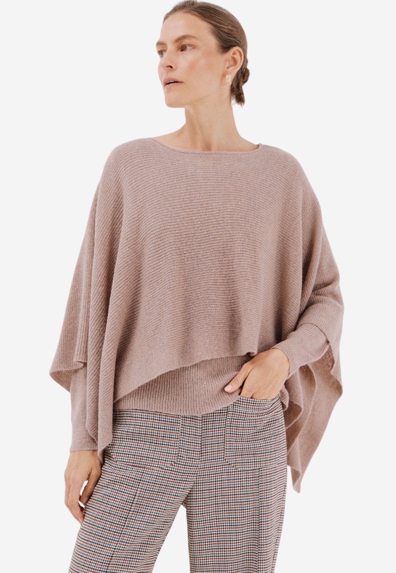 Světle růžový oversized pletený svetr se elegantně splétá, má ribbované textury a široké rukávy, a je spárován s kostkovanými kalhotami na míru.