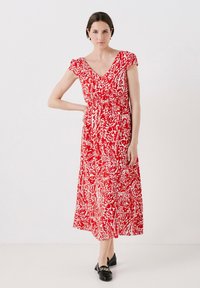Rode maxi jurk met witte bloemen- en paisleypatroon, korte mouwen, getailleerde taille en vloeiende rok. Gestyled met zwarte loafers.