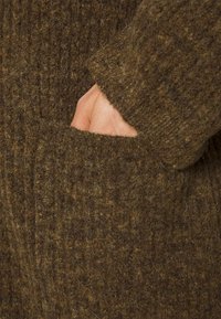 Brauner gestrickter Cardigan mit einem gerippten Muster und einer sichtbaren Tasche. Das Material wirkt weich und warm mit einem leicht flauschigen Finish.