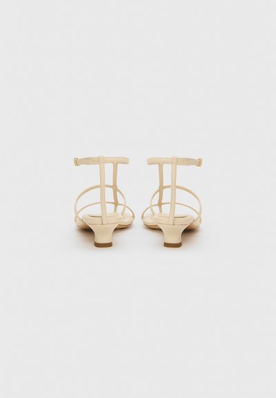 Sandalias beige de tiras con un bajo tacón cuadrado. Presenta tiras finas y un hebilla ajustable en el tobillo. Material suave y diseño minimalista.