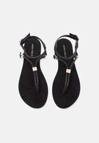 Juodos šlepetės su tekstūruotu, iškylusiu diržu. Turi plokščią padą ir auksinius aksesuarus. Patvarus dirbtinio suede medžiaga.