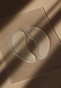 Transparante gel-oogpatches met een glad, gebogen profiel, voorzien van een lichtblauwe rand en subtiele textuur, weergegeven op een vlakke ondergrond.