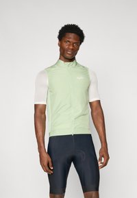 Hellgrüne Radweste mit hohem Kragen und Reißverschluss vorne, kombiniert mit einem kurzärmeligen Mesh-Shirt und schwarzen gepolsterten Shorts.