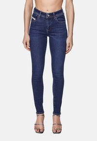 Tunna mörkblå jeans med hög midja, femfickdesign och subtila sömnadsdetaljer. I kombination med sandaletter med klack och remmar.