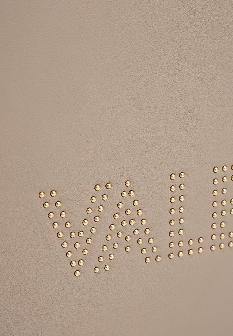 Cuero sintético beige con tachuelas doradas en relieve formando la palabra "VAL". Textura suave, diseño moderno y patrón de letras claro.