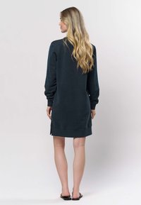 Dunkelblaues Sweatshirtkleid aus weichem Stoff, mit langen Ärmeln, seitlichen Schlitzen und einer lockeren Passform, die bis zur Mitte des Oberschenkels reicht.