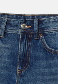 Taille de jean en denim avec passants de ceinture, bouton argenté et poche avant avec coutures orange visibles sur tissu bleu.