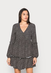 Vestido preto floral com decote em V, mangas longas tipo sino e bainha rendada. O tecido apresenta pequenos padrões florais brancos e rosas por toda a parte.