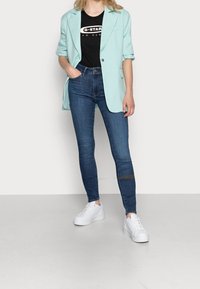 Blazer azul claro sobre una camiseta gráfica negra, combinado con jeans ajustados azul oscuro y zapatillas de plataforma blancas.