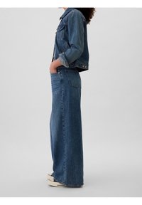 Chaqueta de mezclilla y jeans de pierna ancha en azul medio, con tejido resistente, diseño clásico y un ajuste relajado con bolsillos laterales.