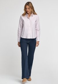 Ljust rosa randig skjorta med knappar och lång ärm, ihop med mörkblå utsvängda jeans och beiga slipskor.