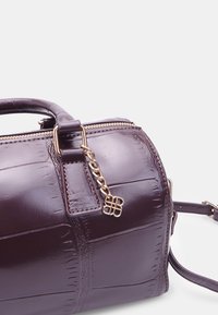 Purple, glossy leather handbag with embossed croc pattern, gold hardware accents, dual handles, and removable shoulder strap. Zipper detail present.