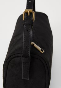 Borsa a mano in suede nero di forma rettangolare, con zip dorata e tracolla rimovibile con fibbia metallica.