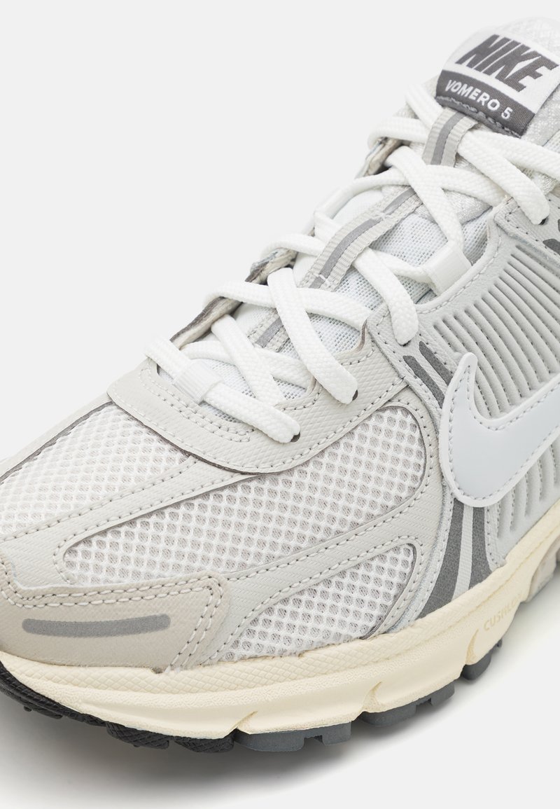 Sneakers Nike Yomero 5 z siateczkowej i syntetycznej cholewki w odcieniach szaro-białych, z kontrastującą czarną podeszwą i wyraźnym logo na języku.