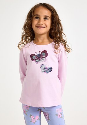 Ανοιχτό ροζ πουκάμισο με μακριά μανίκια, διακοσμημένο με σχέδια πεταλούδων από παγιέτες σε μωβ και μπλε χρώματα. Συνοδεύεται από μπλε κολάν με λουλουδάτα μοτίβα.