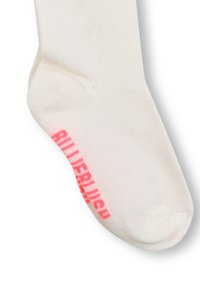 Calzino color crema con una trama a coste, con scritte di un brillante colore rosa sul lato. Il design include un tallone e una punta rinforzati.
