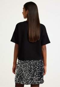 Sort oversized t-shirt med korte ærmer parret med en sort miniature nederdel med palietter, der har skinnende metalliske detaljer og en struktureret overflade.