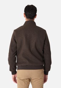 Giacca bomber marrone, con texture, alta colletto, polsini e fascia in costina. Design classico con cuciture visibili e senza decorazioni.