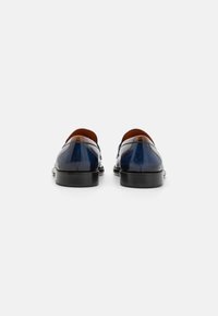 Mocassins en cuir bleu marine avec une finition lisse, accents marron au talon et un bout arrondi. Semelle en caoutchouc noire et design élégant.