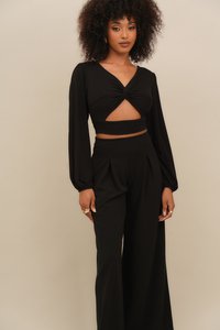 Black cropped top with long puff sleeves, twisted front detail and cutout. Matching high-waisted wide-leg pants, smooth fabric, minimal embellishments.