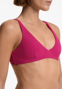 Fuchsiový bikiny top s výstřihem do V, širokými ramínky, texturovanou tkaninou a bezproblémovým zakončením, které zdůrazňuje hladký tvar na pleti.