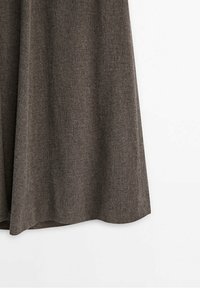 Jupe en laine marron suspendue sur un fond blanc, montrant la texture et le drapé du tissu.