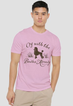 Young man wearing light pink t-shirt with black poodle graphic and text "Oy with the Poodles Already" on front, beige shorts, neutral background.