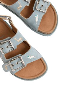 Helleblaue Sandalen mit zwei verstellbaren silbernen Schnallen. Mit gestickten Meeres Tieren und einem weichen braunen Fußbett. Flaches Design und offene Zehen.