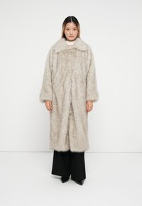 Cappotto in eco-pelliccia color beige chiaro, con un ampio colletto, maniche lunghe e una silhouette morbida. Materiale texturizzato e peloso con una finitura morbida.