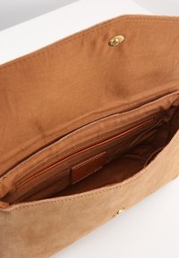 Ruskea mokkanahkainen laukku, jossa pehmeä tekstuuri. Sisällä vaalea vuori, yksi vetoketjullinen tasku ja kultainen painonappi.