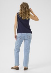 Marinblå ärmlös topp med avslappnad passform, i kombination med ljusblå raka jeans som har bakfickor och ljusa söm detaljer.