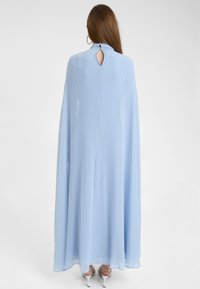 Světle modré maxi šaty vyrobené z jemného šifonu, s výstřihem ve tvaru klíče, vysokým výstřihem a širokými rukávy. Elegantní design pro formální příležitosti.