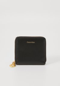 Portefeuille en cuir noir avec une fermeture éclair dorée et un logo, de forme rectangulaire, texture lisse, avec un accent en métal en forme de cœur.