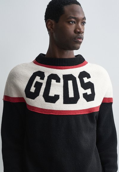 Suéter de punto negro con un patrón de rayas blancas y rojas, con "GCDS" en letras negras en negrita en el pecho. Diseño de cuello redondo.