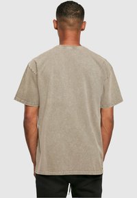 Tricou oversized gri deschis, cu mâneci scurte, guler rotund și un material moale, ușor texturat. Cusăturile sunt lucrate subtil.