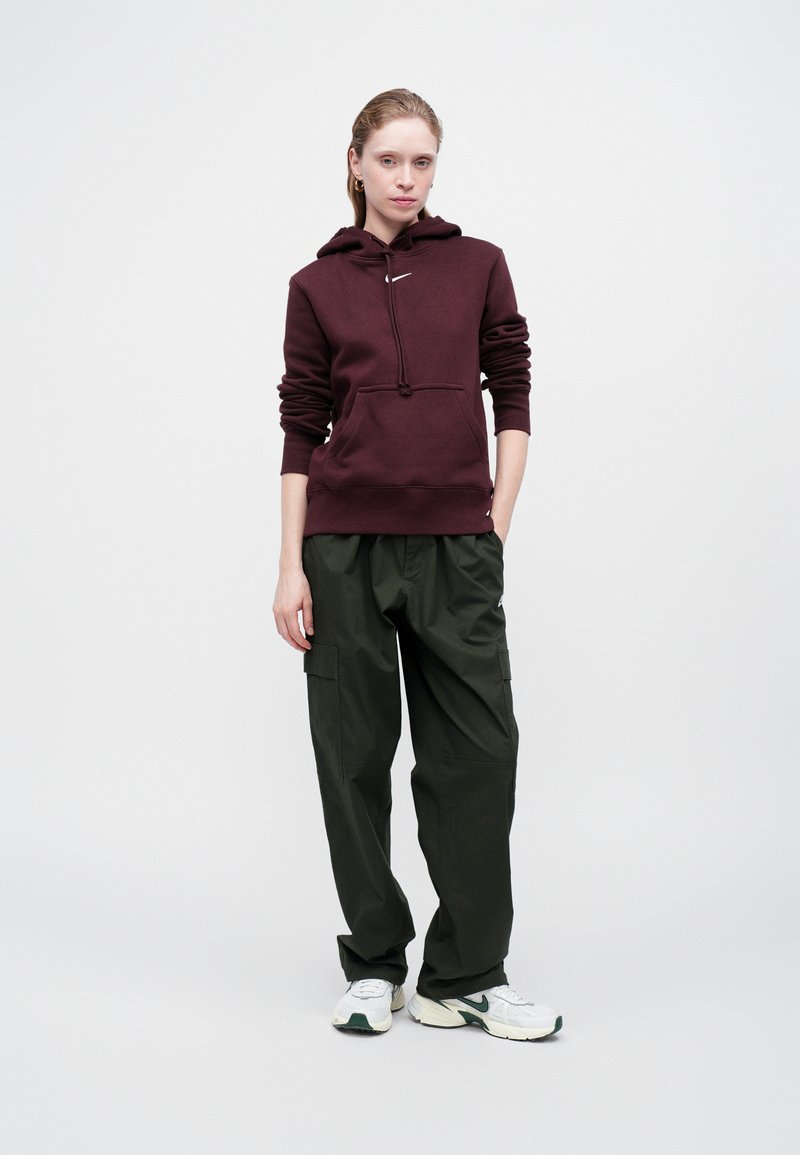 Sweatshirt capuz bordeaux com bolso frontal, combinado com calças cargo verdes-azeitona de corte largo. O modelo usa ténis brancos com detalhes verdes.