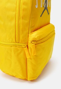 Zaino giallo con tessuto testurizzato, dotato di un compartimento principale e di una tasca frontale più piccola, entrambe con zip gialle coordinate.