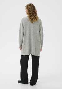 Grå stickad cardigan med ett strukturerat mönster, långa ärmar och en avslappnad passform, ihop med svarta vida byxor.