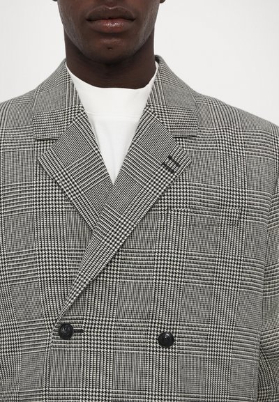 Doppelt gefütterte Blazer in einem schwarz-weißen Karomuster. Verfügt über breite Revers und zwei schwarze Knöpfe. Hergestellt aus strukturiertem Stoff.