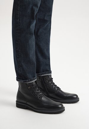 Czarne skórzane botki za kostkę z okrągłymi noskami, sznurowanym designem, teksturowaną powierzchnią i gumowymi podeszwami, w połączeniu z ciemnoniebieskimi dżinsami.