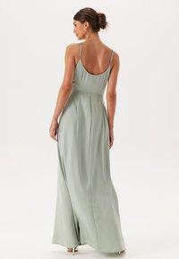 Dlouhé, bezramínkové šaty ze světle zelené látky; mají přiléhavý korzet, splývavou sukni a jemné popruhy s nastavitelného kováním.
