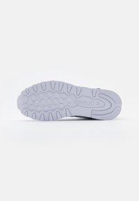 Sole of light gray Reebok sneaker with circular and rectangular tread patterns and Reebok logo embossed in the center.
