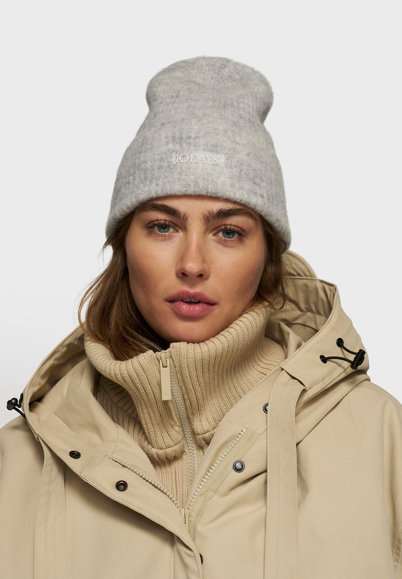 Berretto grigio lavorato a maglia con orlo arrotolato e testo ricamato. Giacca beige con zip, colletto alto e strato interno in maglia a costine.