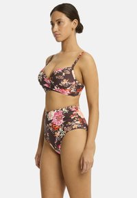 Il modello posa di lato in un bikini floreale con uno sfondo marrone, mettendo in mostra un top aderente e un paio di mutande a vita alta. Styling semplice ed elegante.