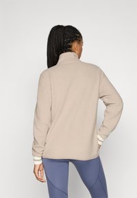 Beige fleece pullover med høj krave, der har lange ærmer og stribede manchetter. Stoffet har et blødt, struktureret udseende.