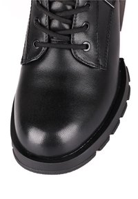 Gros plan sur une botte en cuir noire avec un bout arrondi, des lacets noirs et une semelle en caoutchouc épaisse avec un motif de bande de roulement profond.