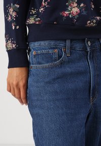 Námořnický květinový svetr s manžetami, zkombinovaný s modrými džíny, které mají měděné nýty a klasický design s pěti kapsami.
