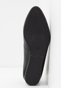 Chaussure en cuir noir avec une semelle en caoutchouc texturée. Le design est élégant et épuré, mettant en avant un style minimaliste sans ornements.