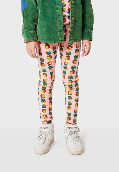 Värikylläiset leggingsit, joissa on vaaleanpunainen tausta ja monivärisiä noppa-kuvioita. Mallilla on yllään vihreä corduroypaita ja valkoiset tennarit.